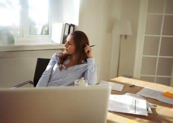 Young businesswoman looking away in thought while sitting at her desk with laptop. Beautiful young female working from home office.
